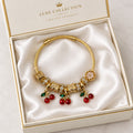 Gold twisted cable charm bangle bracelet with red enamel cherry charms, gold filigree beads, and white flower accent