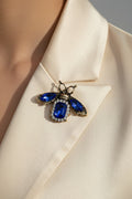 Blue sapphire crystal bee brooch with white rhinestone accents on display card