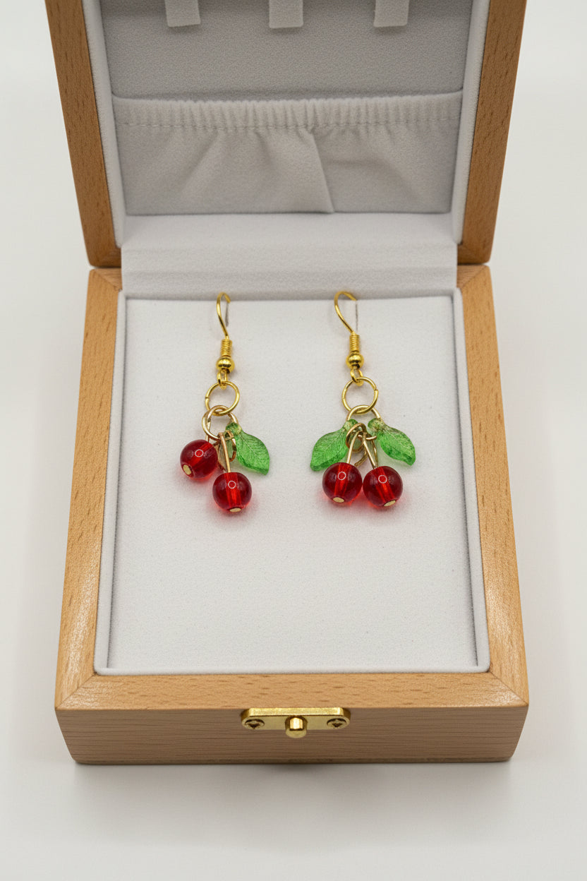 Cherry beaded dangle earrings with red glass beads and green leaf charms on gold-tone fish hook wires