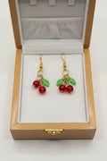 Cherry beaded dangle earrings with red glass beads and green leaf charms on gold-tone fish hook wires
