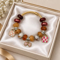 Gold twisted cable charm bangle bracelet with brown and burgundy beads, enamel handbag charms, and pink bow charm