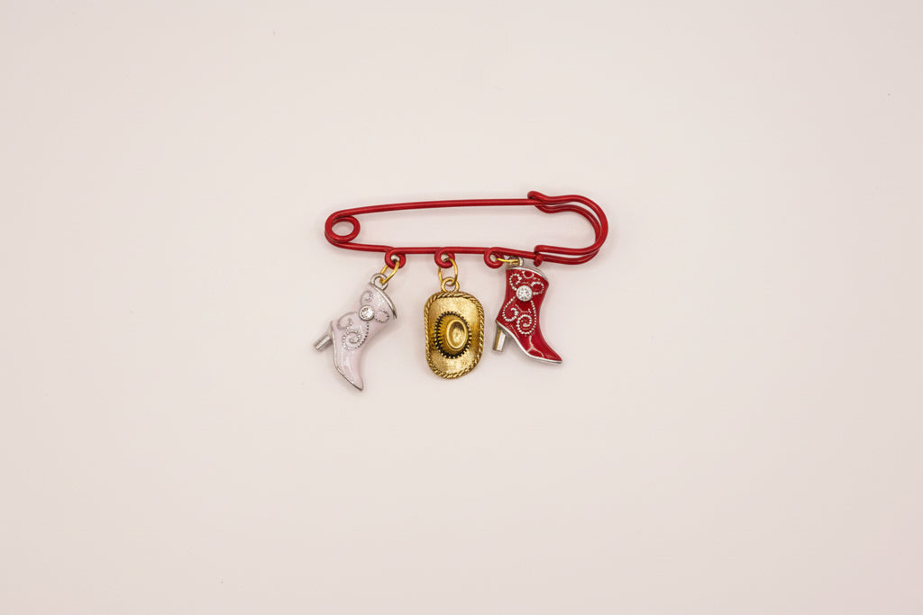 Handmade red safety pin with silver and red cowboy boot charms and gold sombrero hat on a kraft Handmade display card